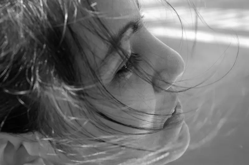 A black-and-white portrait of a woman in profile, her hair blowing across her face.