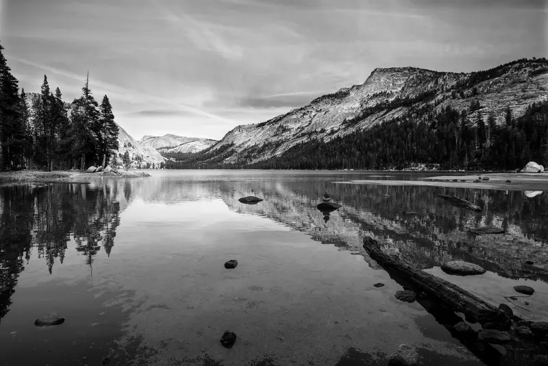 A still mountain lake reflecting granite peaks and pines, in black and white.